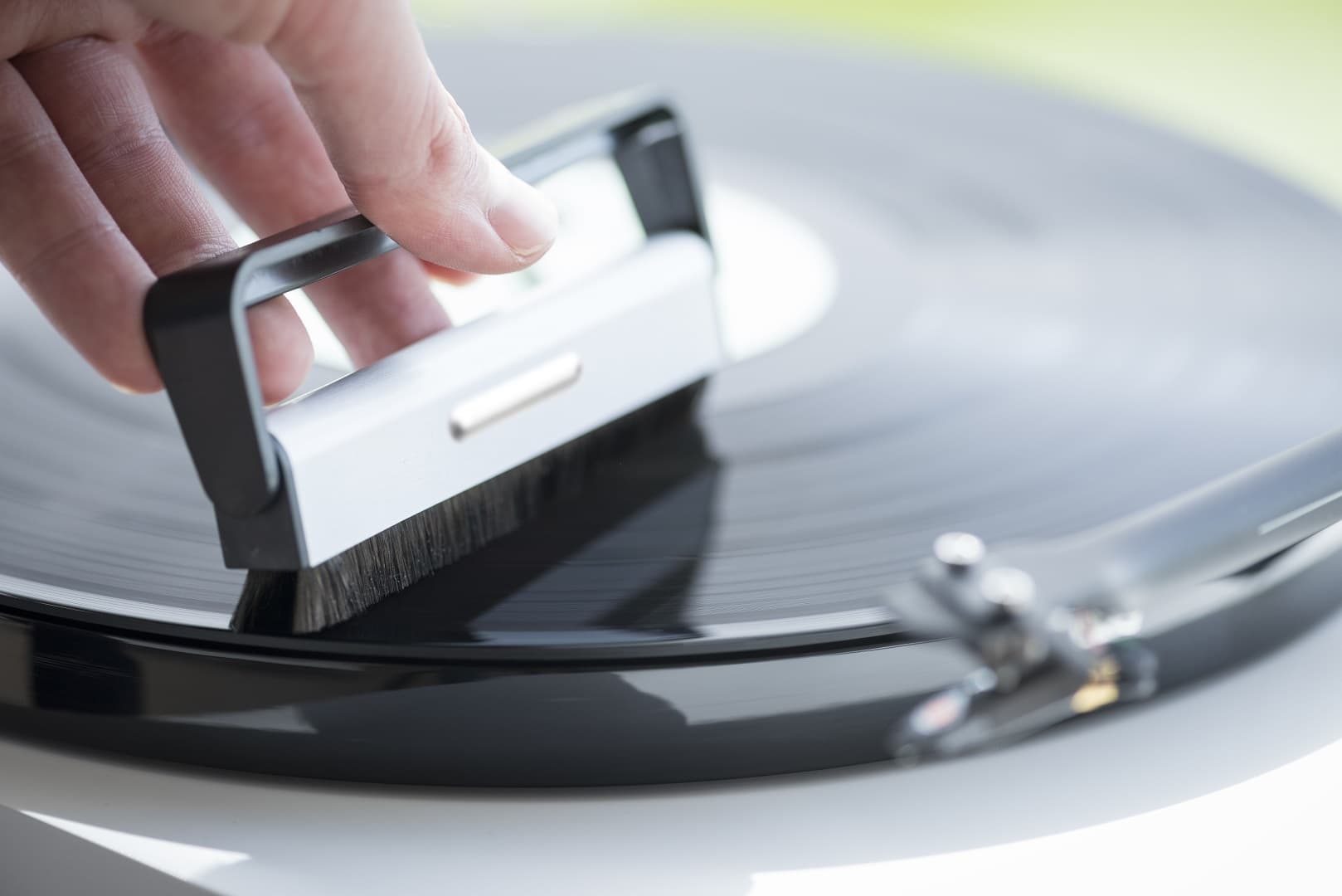 A carbon-fiber brush held lightly against a spinning record, lifting dust from the grooves.