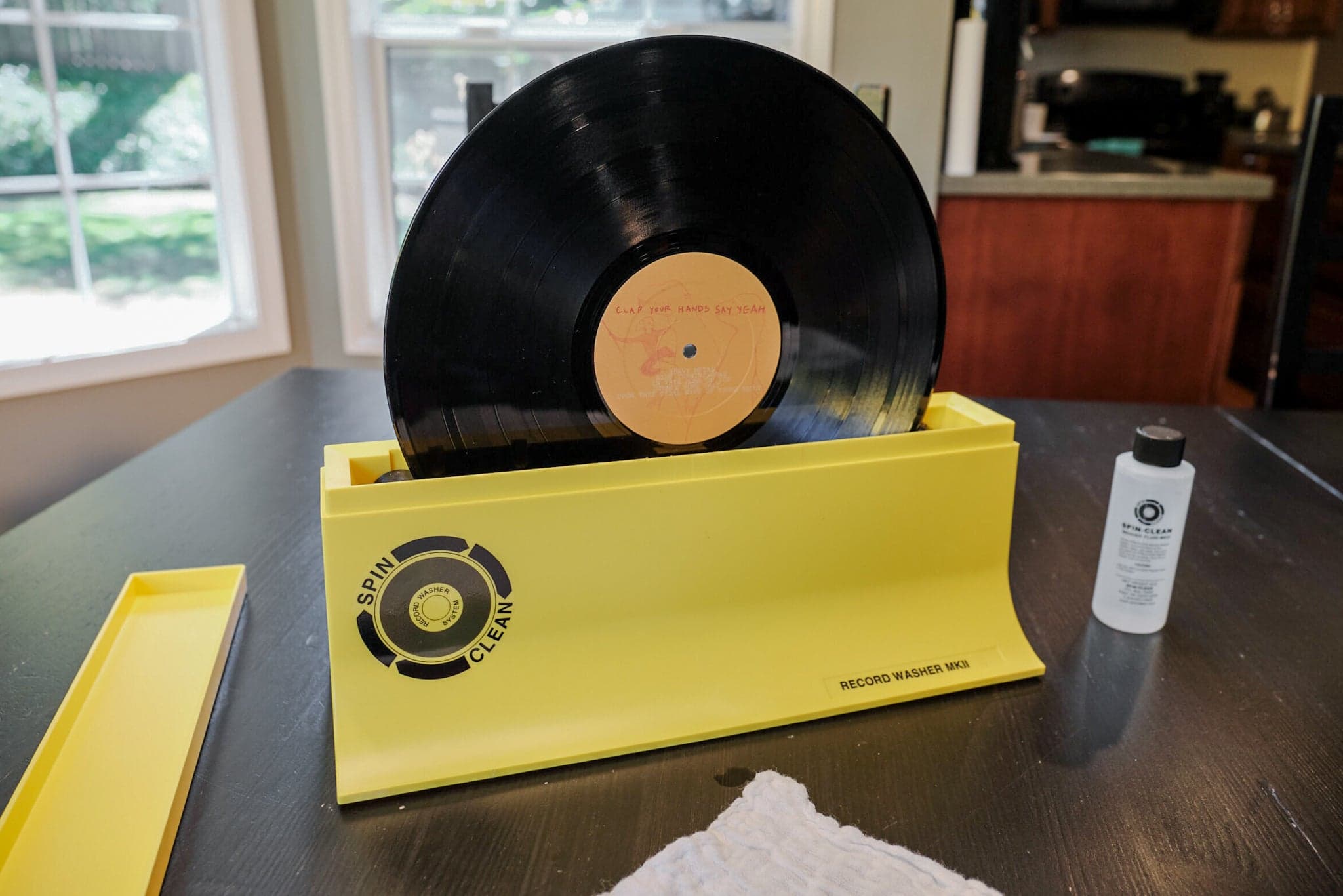 A record being turned through a manual bath-style cleaner, both sides passing through the velvet brushes at once.