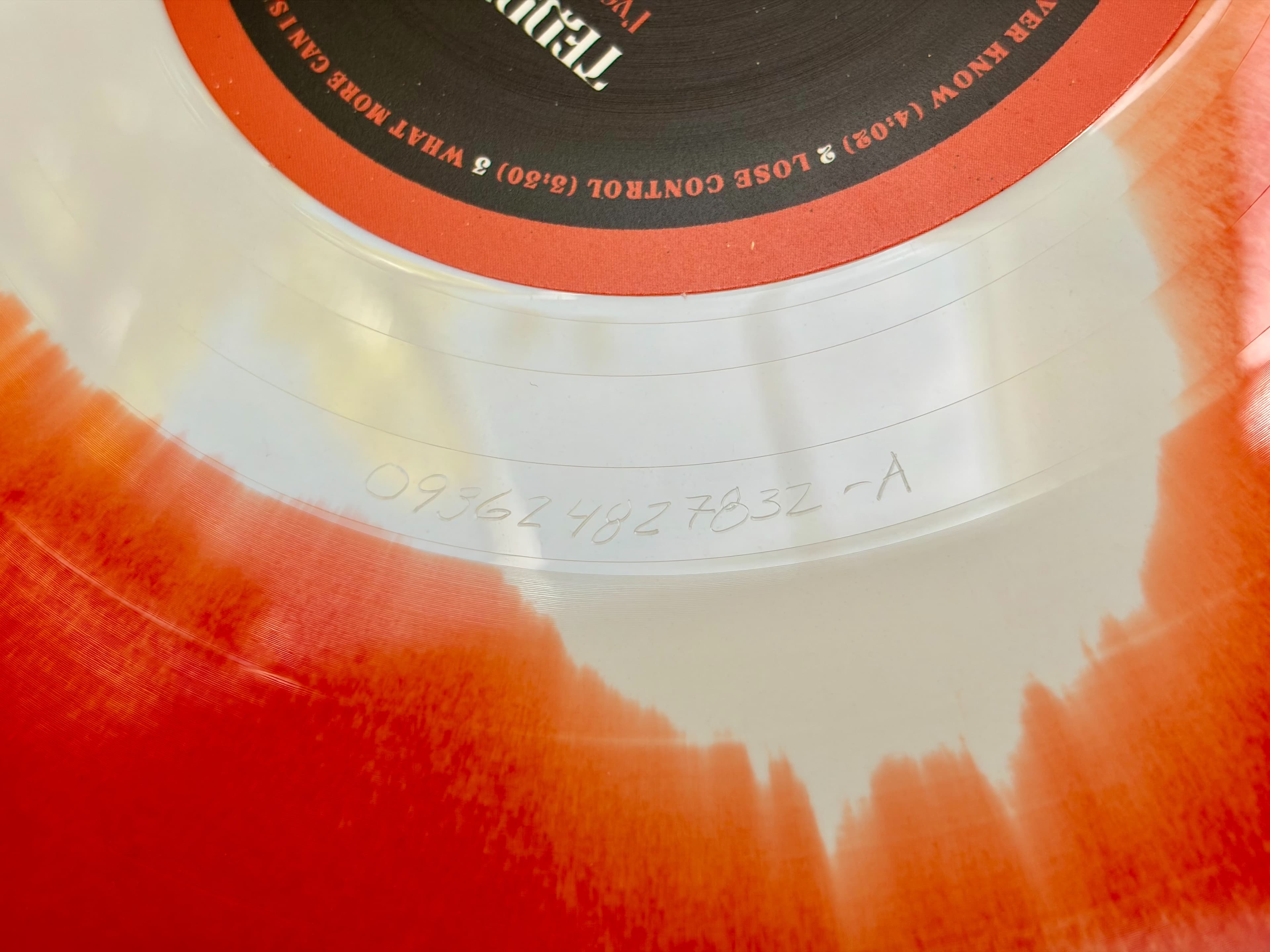 The deadwax of a record tilted under a raking light, with the matrix code etched into the smooth ring between the last groove and the label.